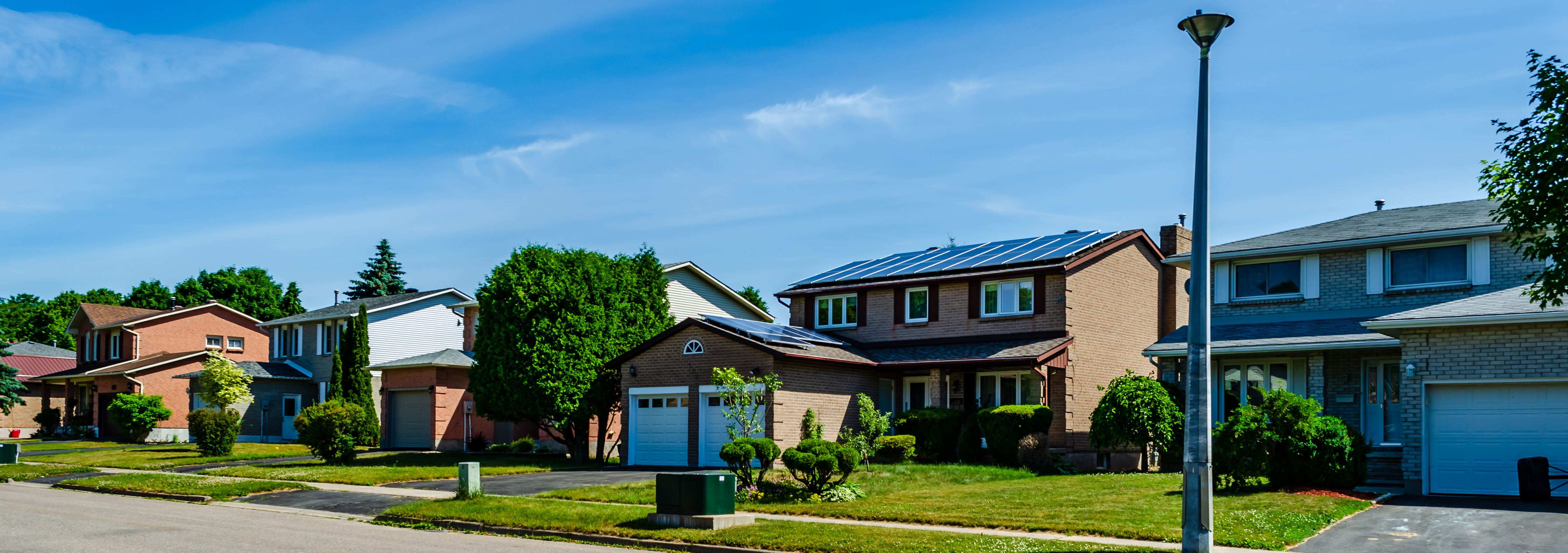Panorama of a row of residential houses along a street, one with solar panels on the roof under a blue sky